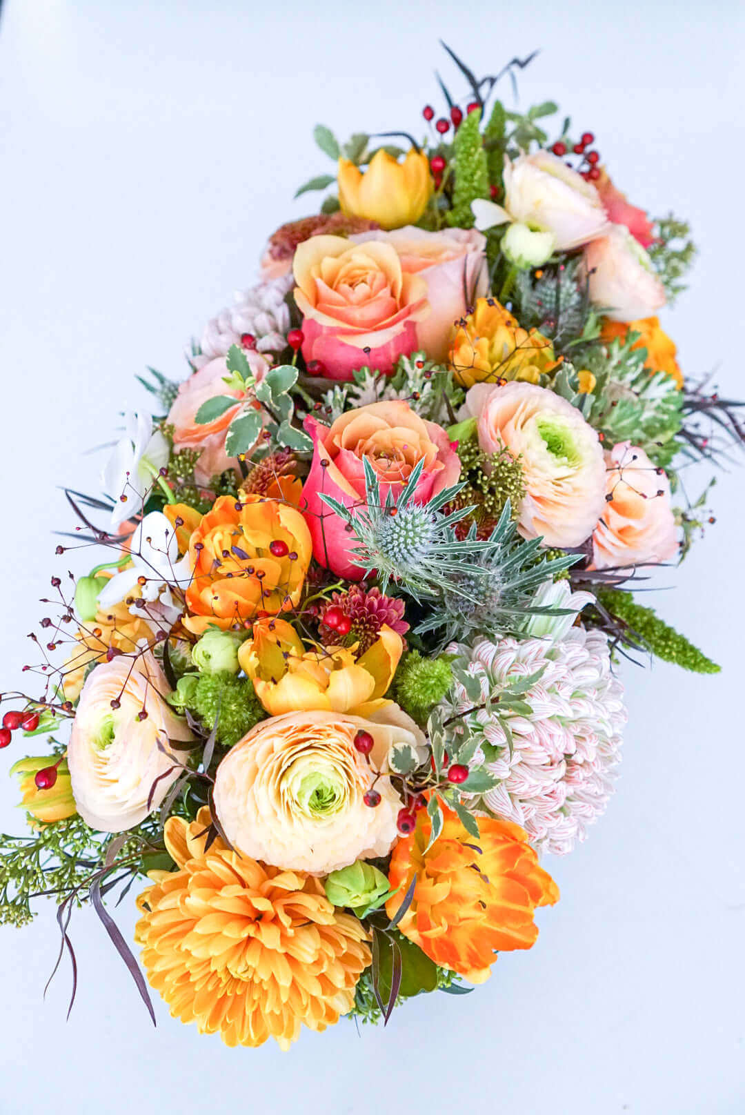 Add some glow to your Thanksgiving dinner table or fall-decorated foyer with this warm, seasonal arrangement. This Thanksgiving centerpiece features candy crush commercial mum, bi-colour roses, bronze mum, cabbage bloom, peach ranunculus, rosehips, and bronze tulips.