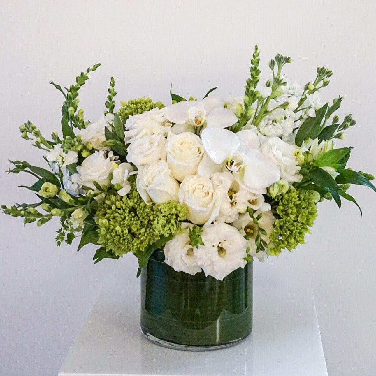 Blooms of bright white, cream and lime green. The combination is rich with texture and innocent beauty. Presented in a 6x6" cylinder glass vase that they will use later for roses, tulips, potpourri, etc.
