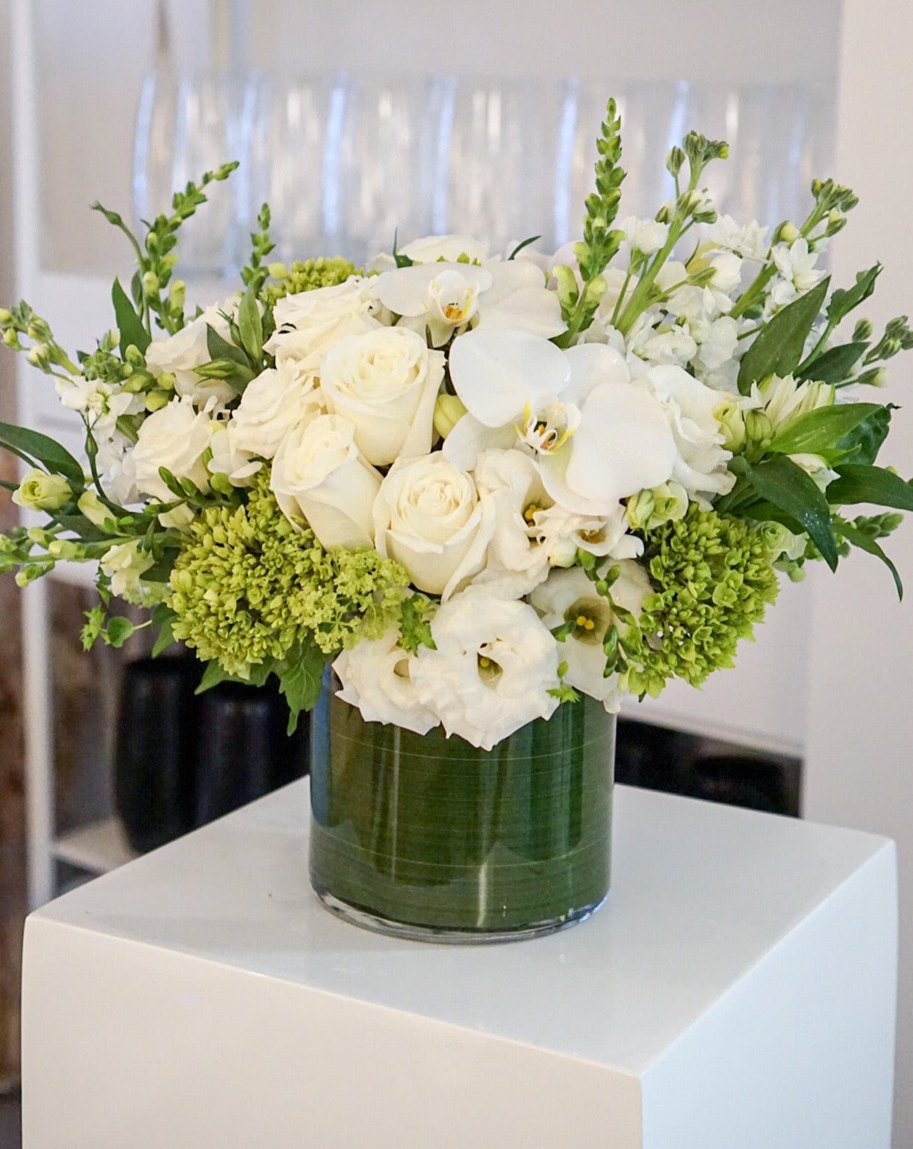 Blooms of bright white, cream and lime green. The combination is rich with texture and innocent beauty. Presented in a 6x6" cylinder glass vase that they will use later for roses, tulips, potpourri, etc.