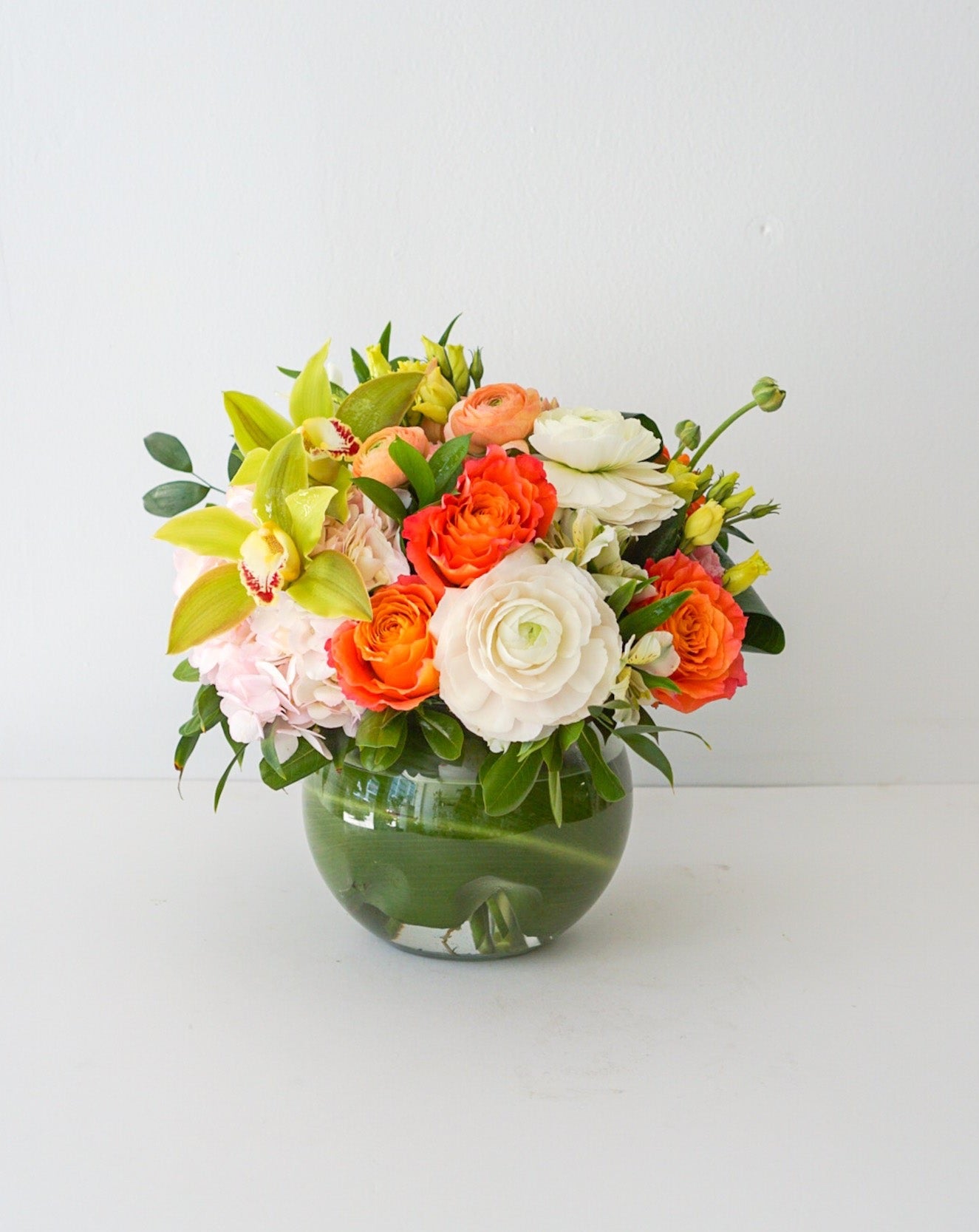 A fun-filled play on colours. The arrangement contracts pretty pink, peach, orange, green and white blooms with a fish bowl glass vase that sure to become multi purpose decor item.