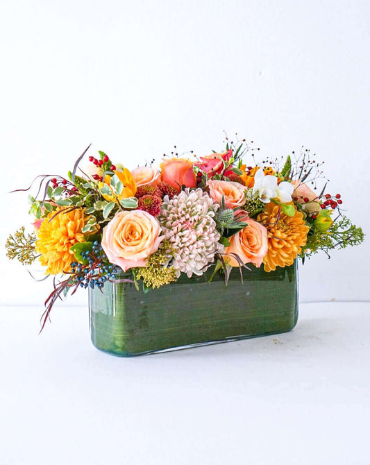 Add some glow to your Thanksgiving dinner table or fall-decorated foyer with this warm, seasonal arrangement. This Thanksgiving centerpiece features candy crush commercial mum, bi-colour roses, bronze mum, cabbage bloom, peach ranunculus, rosehips, and bronze tulips. 