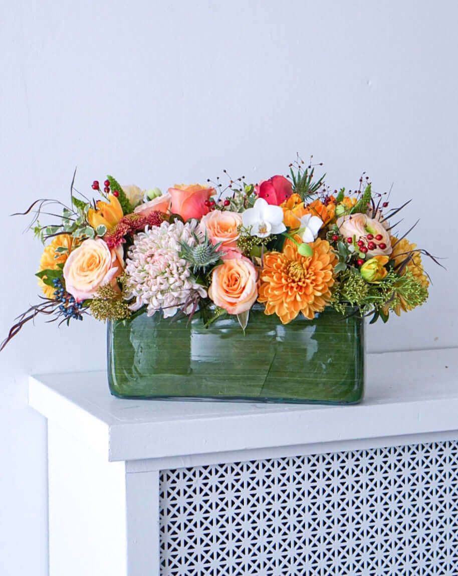 Add some glow to your Thanksgiving dinner table or fall-decorated foyer with this warm, seasonal arrangement. This Thanksgiving centerpiece features candy crush commercial mum, bi-colour roses, bronze mum, cabbage bloom, peach ranunculus, rosehips, and bronze tulips. 