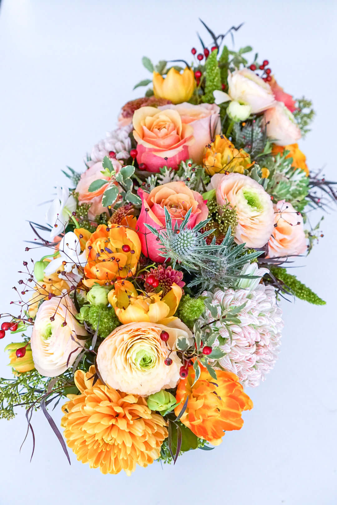 Add some glow to your Thanksgiving dinner table or fall-decorated foyer with this warm, seasonal arrangement. This Thanksgiving centerpiece features candy crush commercial mum, bi-colour roses, bronze mum, cabbage bloom, peach ranunculus, rosehips, and bronze tulips. 