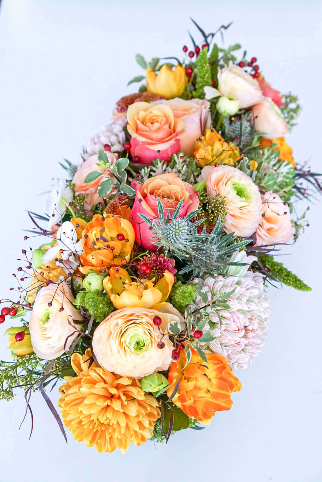 Add some glow to your Thanksgiving dinner table or fall-decorated foyer with this warm, seasonal arrangement. This Thanksgiving centerpiece features candy crush commercial mum, bi-colour roses, bronze mum, cabbage bloom, peach ranunculus, rosehips, and bronze tulips. 