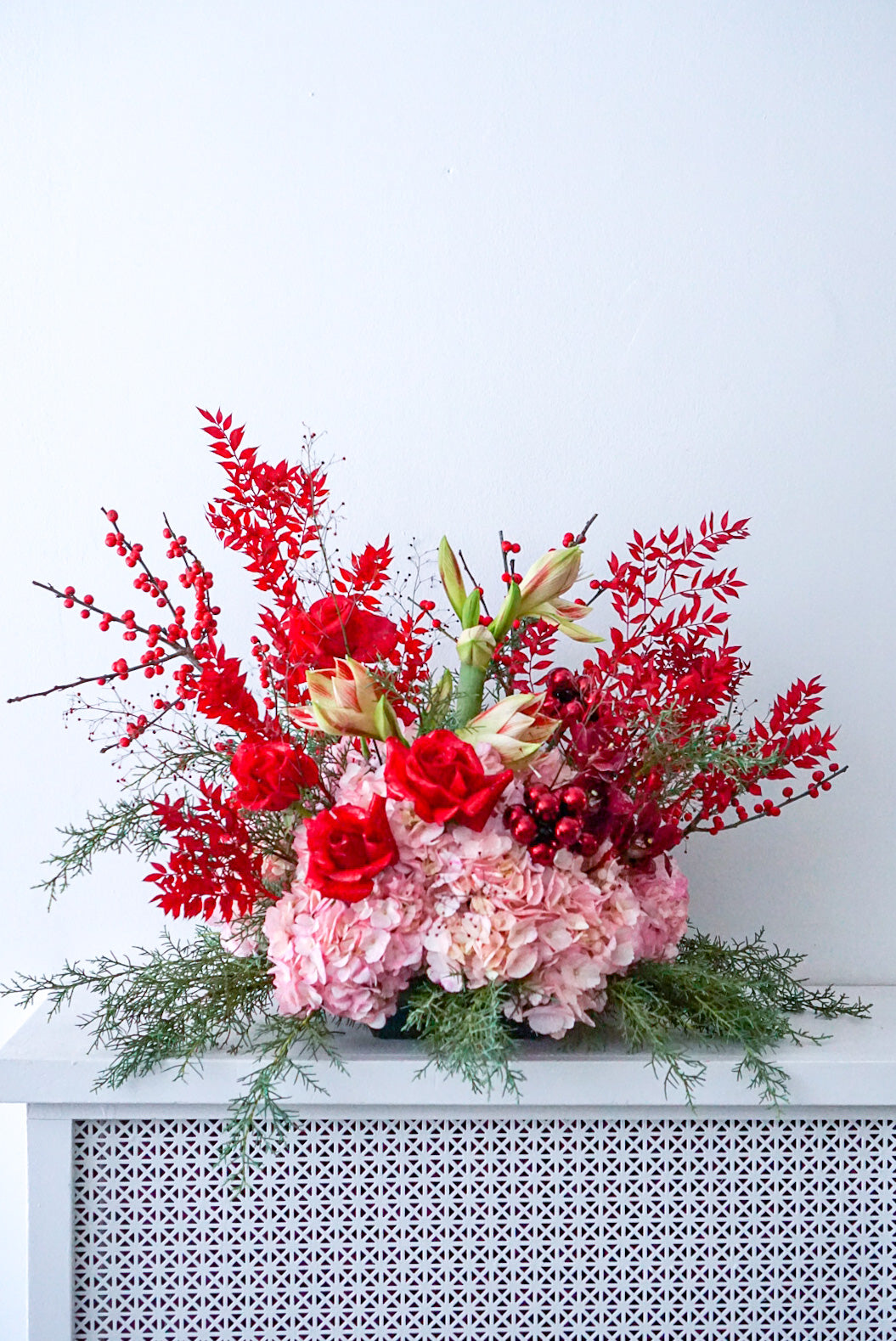 “Holiday floral arrangement with red amaryllis, pink hydrangeas, and ilex berries by The Flower Nook”