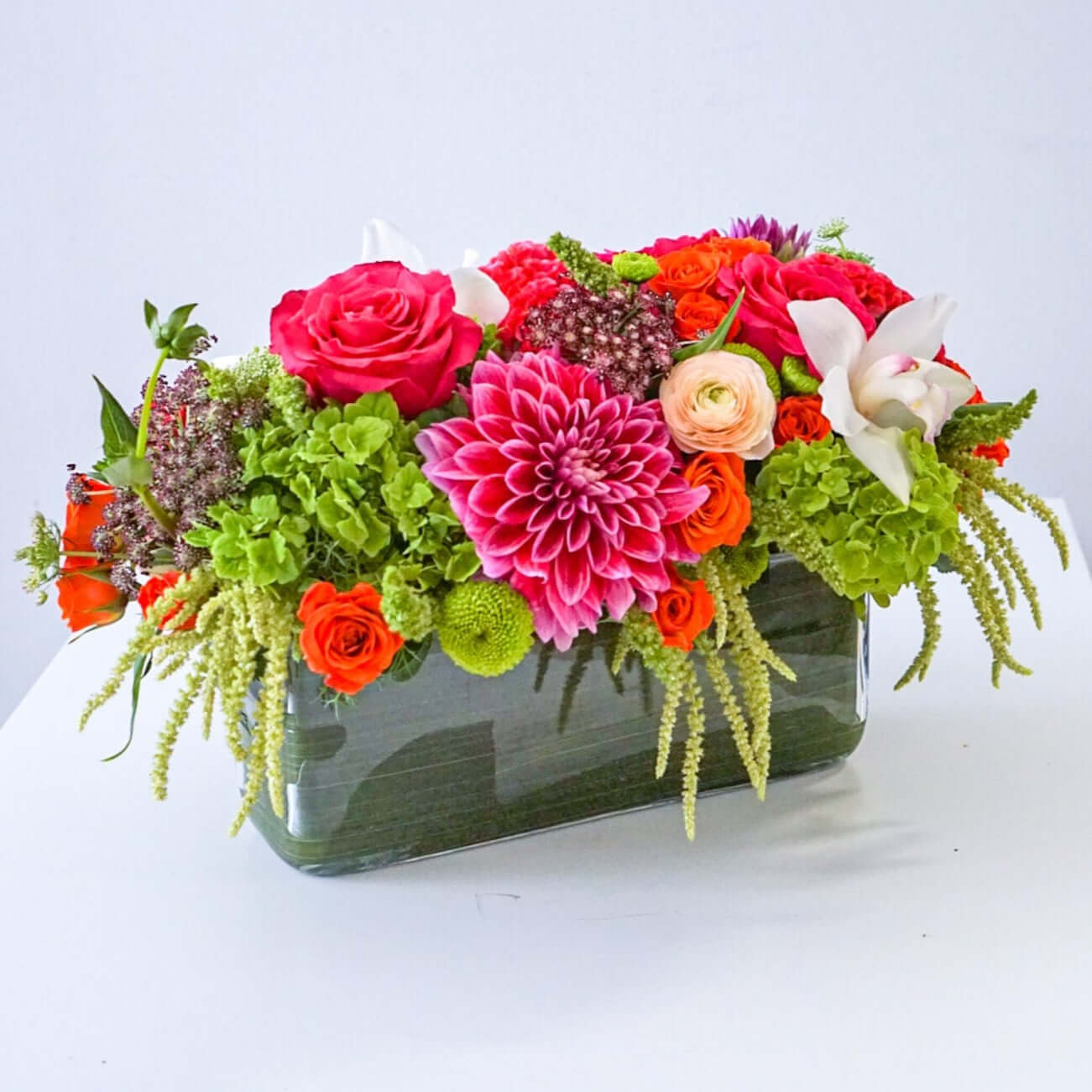 A centrepiece full of the fall's best blooms. Featured: green hydrangeas, free spirit roses, dahlias, cymbidium orchids, spray roses, designed in a 12" rectangle clear glass leaf-lined cylinder.