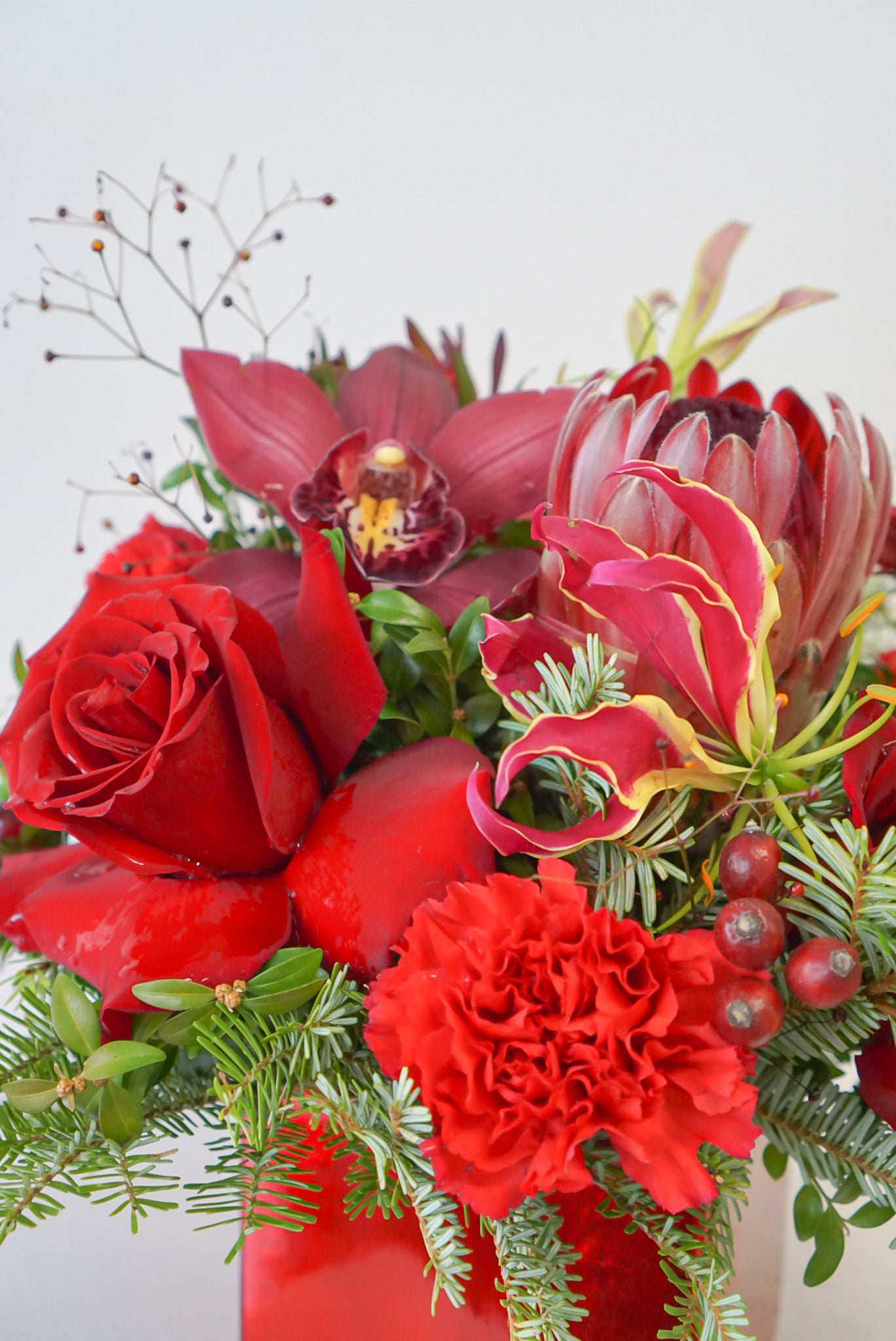 Bring your holiday table to life with this beautiful all red blooms flower arrangement. A charming display of protea, freedom roses, gloriosa, with a fragrant assortment of winter evergreen. Flower Nook, Toronto Florist