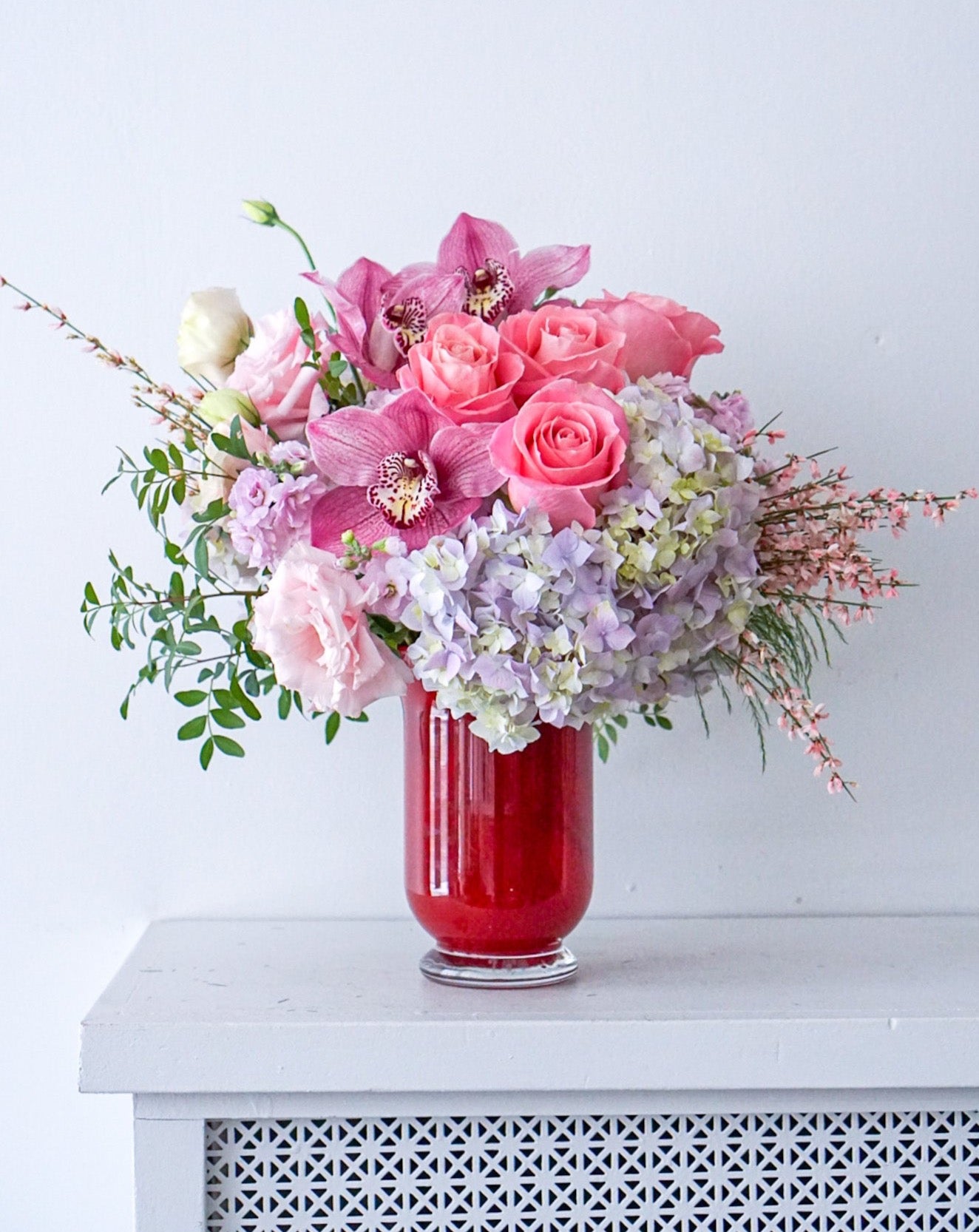 In the prettiest shades of pink, this breathtaking arrangement proclaim your affection in the most adorable way!   This  arrangement includes premium pink hydrangeas, roses, cymbidium orchid, stocks, etc. Designed in a red cherry glass vase 