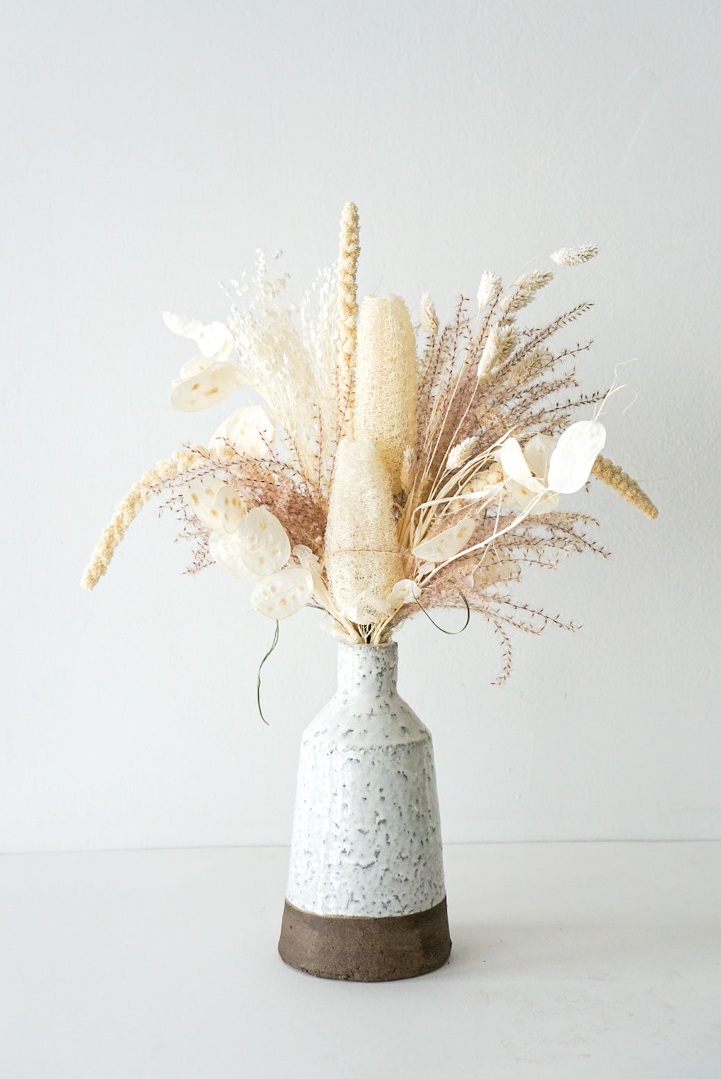 Moments-in-time This beautiful dried flower arrangement includes all the interesting elements and texture such as - bunny tails, pampas grass, eucalyptus. Created in a stunning hand-made ceramic pot. 