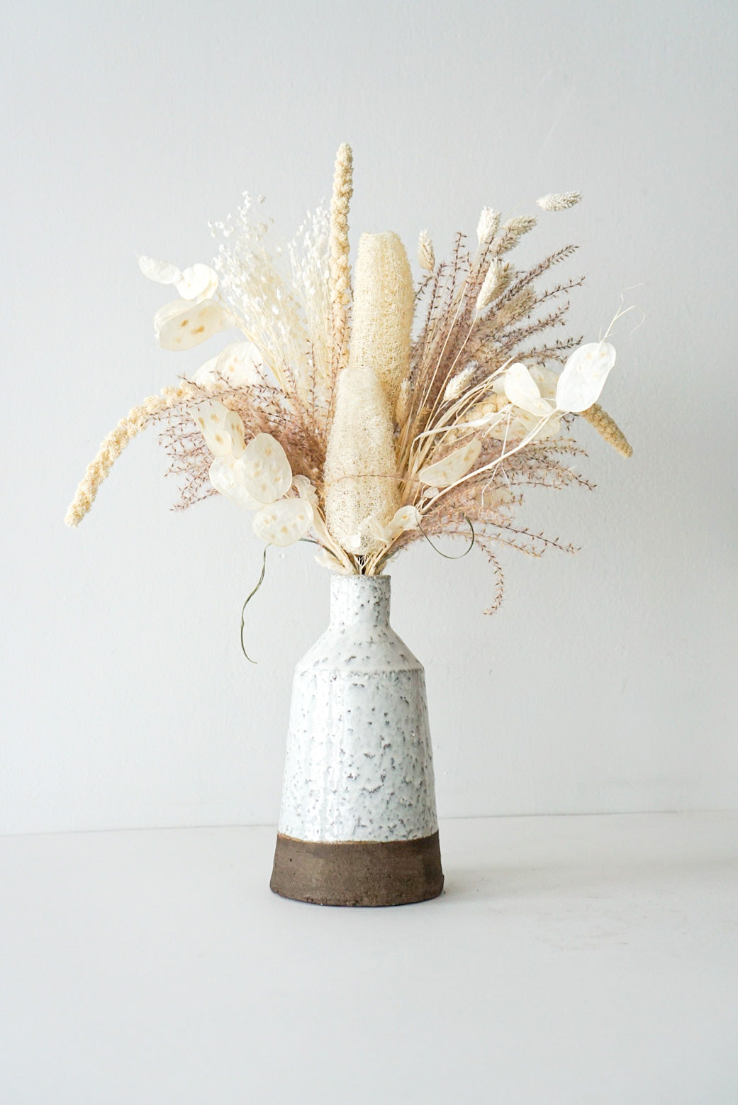 This beautiful dried flower arrangement includes all the interesting elements and texture such as - bunny tails, pampas grass, eucalyptus. Created in a stunning hand-made ceramic pot. 
