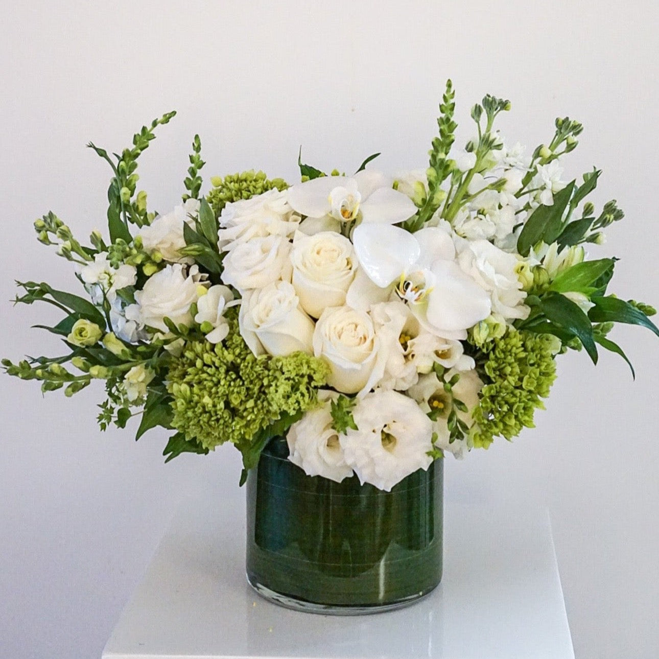Blooms of bright white, cream and lime green. The combination is rich with texture and innocent beauty. Presented in a 6x6" cylinder glass vase that they will use later for roses, tulips, potpourri, etc. 