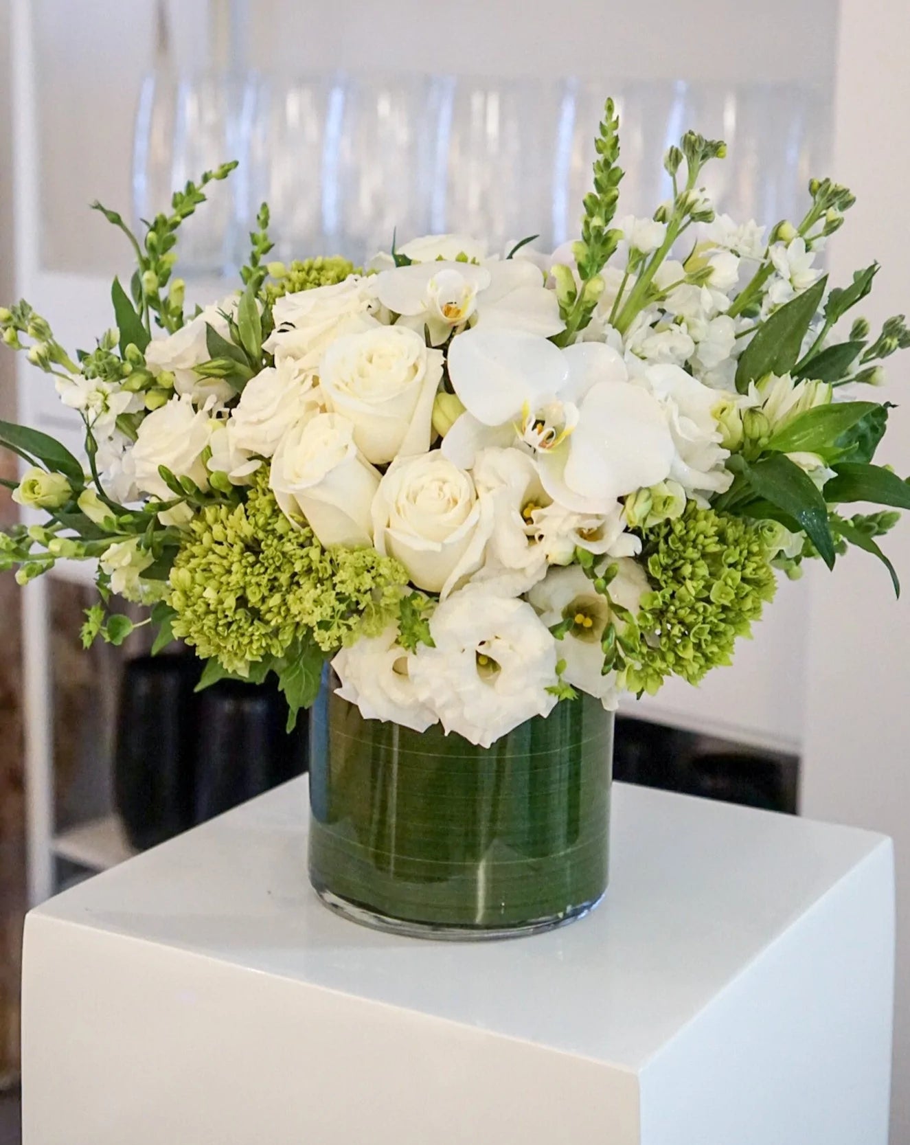 Blooms of bright white, cream and lime green. The combination is rich with texture and innocent beauty. Presented in a 6x6" cylinder glass vase that they will use later for roses, tulips, potpourri, etc. 