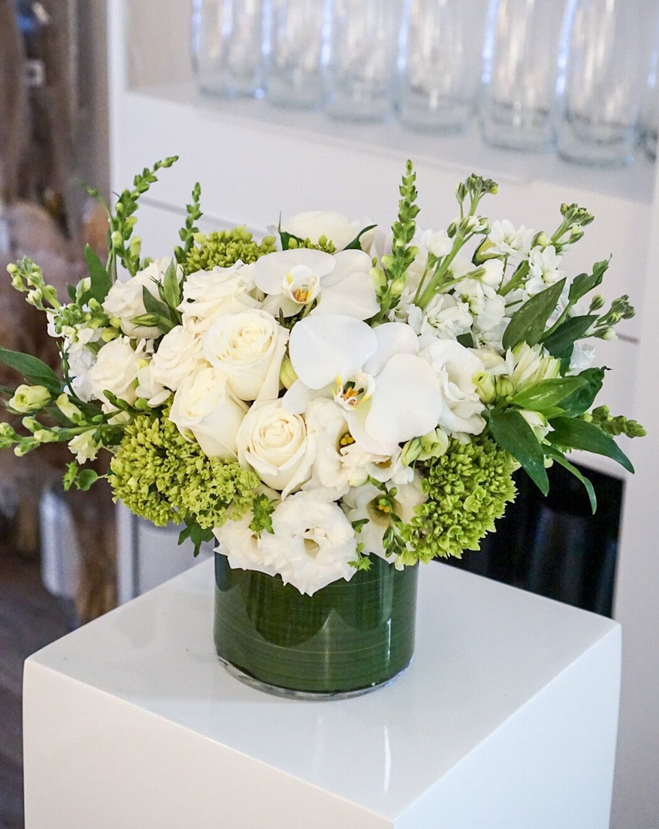 Blooms of bright white, cream and lime green. The combination is rich with texture and innocent beauty. Presented in a 6x6" cylinder glass vase that they will use later for roses, tulips, potpourri, etc. 